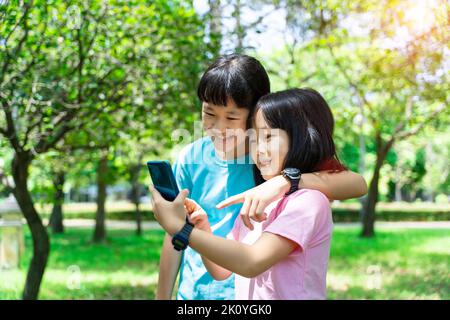 Two sisters hugging while using mobile phone in the park. Happy family concept. Stock Photo