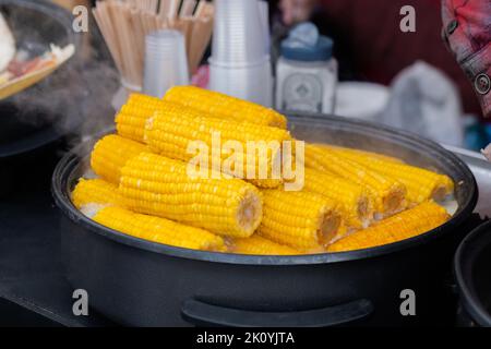 Close up: process of cooking yellow corn cobs in saucepan at outdoor food market Stock Photo
