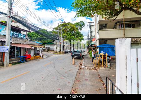 CHIANG MAI, THAILAND - 4.11.2019: Street in the Chiang Mai city. Street view with cars, wooden houses, trees. Narrow road in the middle. Stock Photo
