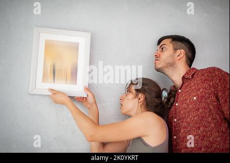 Cheerfully young couple decorates their new apartment with painting on the wall Stock Photo