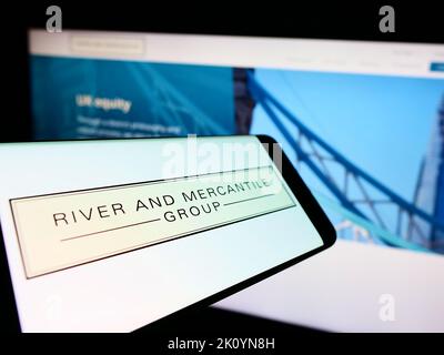 Mobile phone with logo of company River and Mercantile Group Limited on screen in front of business website. Focus on center of phone display. Stock Photo