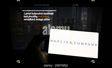 Person holding smartphone with logo of US investment firm Moelis and Company on screen in front of website. Focus on phone display. Stock Photo