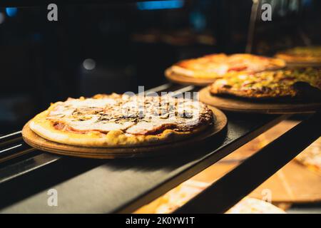 perspective view closeup of different kinds of pizza on wooden plates on the shelves of street food shop window Stock Photo