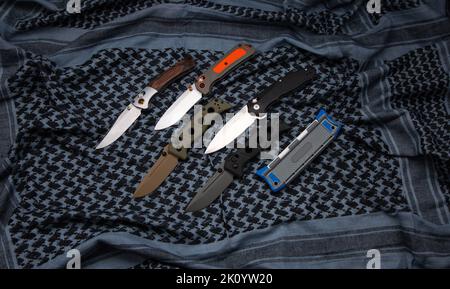 Compact metal sharp knife with a folding blade. Pocket folding knives on a fabric background. Stock Photo