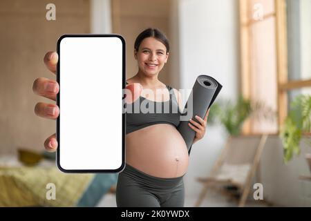 Pregnant Woman With Fitness Yoga Mat In Hand Demonstrating Big Blank Smartphone Stock Photo