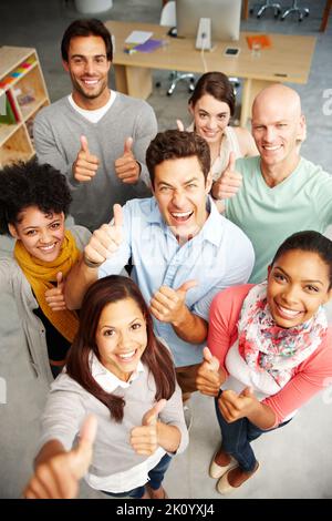 People who are passionate. High angle view portrait of a group of multi-ethnic people holding thumbs up in a work environment. Stock Photo