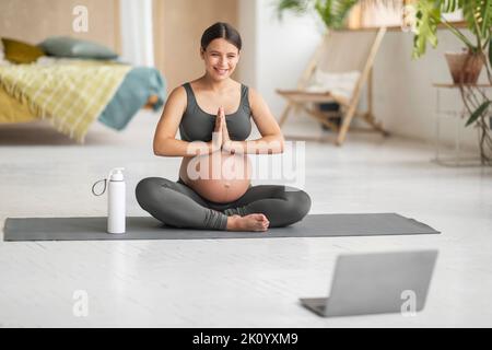 Beautiful Pregnant Woman Having Online Yoga Lesson With Laptop At Home Stock Photo