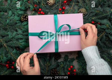 female hands untie ribbon on Christmas present against background of dark spruce branches. merry christmas and happy new year. Christmas and New Year Stock Photo