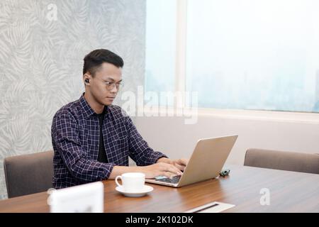 Serious office employee sitting at work desk with laptop, preparing report, making online presentation looking focused at work. The concept of using t Stock Photo