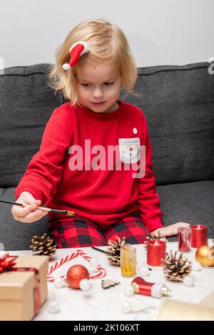 Christmas kids craft activities at home. Little girl wearing holiday pajamas, doing crafts. Christmas tree decorations at home. Holiday DIY concept fo Stock Photo