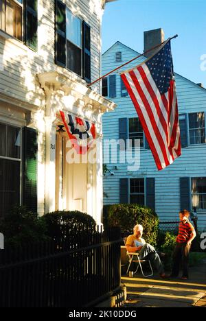 A grandfather and his grandson enjoy a relaxing conversation under an American flag in the front yard of their home on the Fourth of July. Stock Photo