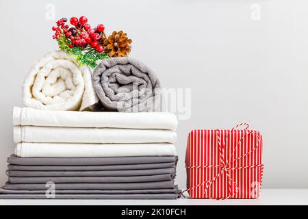 Folded rolls of towels and bed linen, sheets on the table with Christmas decor and a gift. Stock Photo