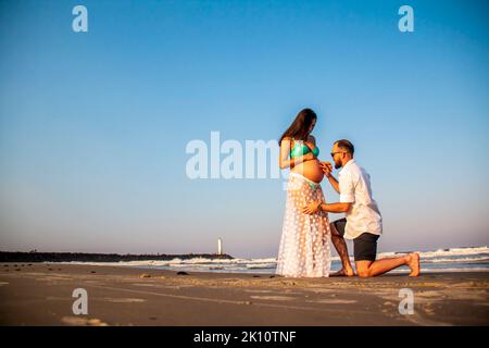 Couple of prospective parents holding hands, walking on the beach Stock Photo