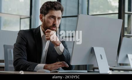 Focused Caucasian bearded adult 40s man CEO company worker manager boss businessman working on computer in office searching solution of problem decide Stock Photo