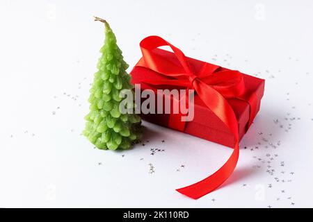 Christmas composition of a red gift box with a red bow and a green Christmas tree candle on a gray background with silver confetti stars Stock Photo