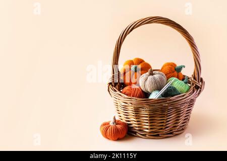 Knitted orange green and beige pumpkins in a basket on a orange background, knitting hobby, autumn composition. Halloween concept. Stock Photo