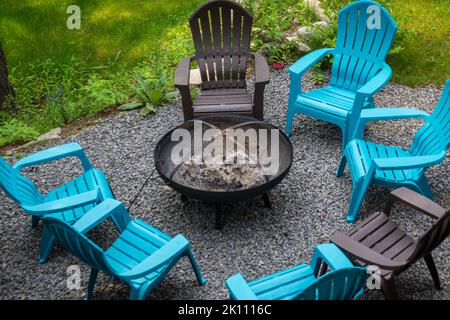 Empty plastic chairs around an extinguished fireplace with ashes, in the backyard of a camping site  Stock Photo