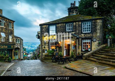 Haworth Main Street (steep hill, old buildings, blue hour evening light, historic Bronte sisters' village, Grade 2 pub) - West Yorkshire, England, UK. Stock Photo