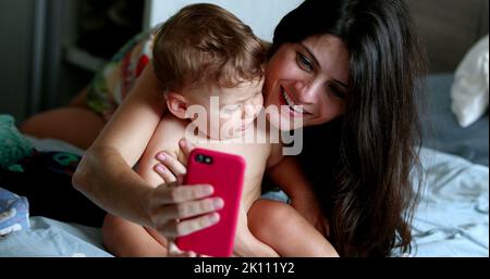 Candid mother taking selfie with infant baby in bedroom at home Stock Photo