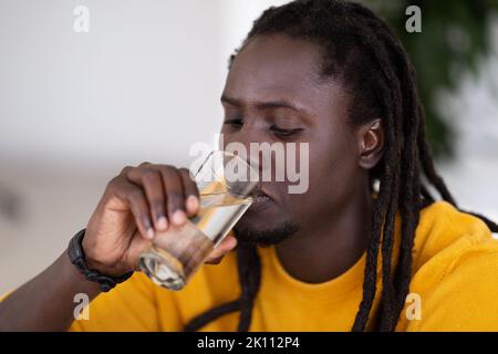 Body Hydration. Young Black Man With Dreadlocks Drinking Water From Glass Stock Photo