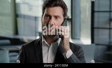 Bearded Caucasian middle-aged adult business man talking phone at office explain negotiate virtual sales conversation using mobile male professional Stock Photo