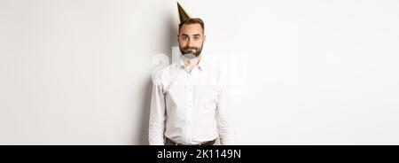 Celebration and holidays. Gloomy guy in birthday hat standing awkward ...