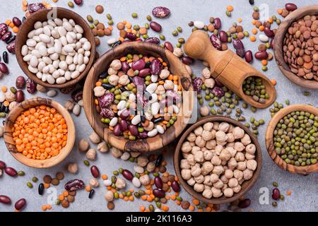Top view of different beans, lentils, mung, chickpeas in wooden bowls for tasty meals on grey concrete background Stock Photo