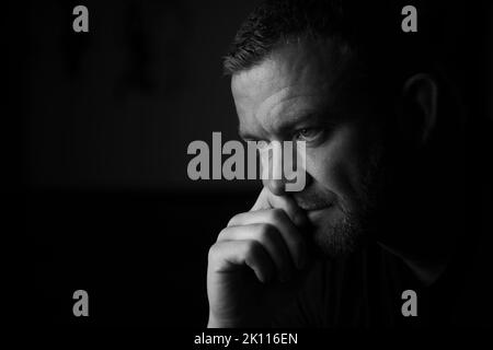 Male sits with hand by mouth in a thinking expression. Stock Photo