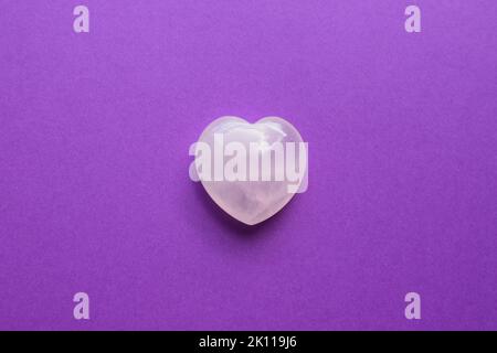 A beautiful heart-shaped rose quartz crystal lies on a lilac background. Rose quartz is a stone for success in love for women. Stock Photo