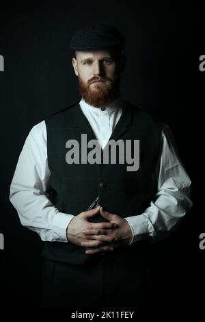 A working class Victorian man with red hair and beard against a black backdrop Stock Photo