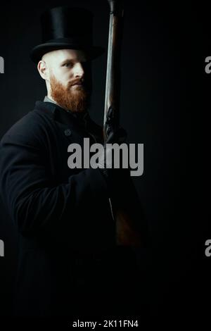 A working class Victorian man with red hair and beard against a black backdrop Stock Photo