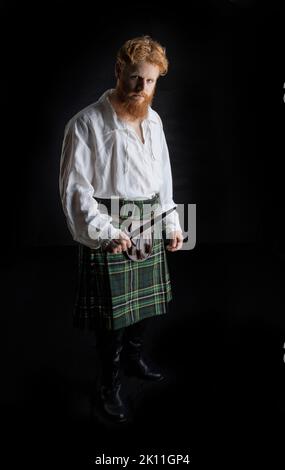 A Scottish man with red hair and beard wearing a kilt  and holding a weapon Stock Photo