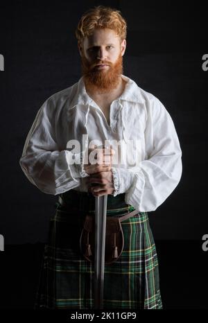 A Scottish man with red hair and beard wearing a kilt  and holding a weapon Stock Photo