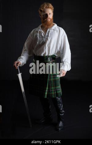 A Scottish man with red hair and beard wearing a kilt  and holding a weapon Stock Photo