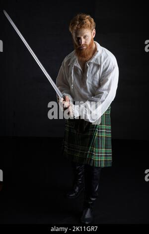 A Scottish man with red hair and beard wearing a kilt  and holding a weapon Stock Photo