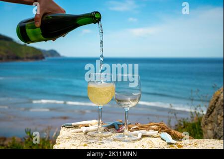 Pouring of txakoli or chacolí slightly sparkling very dry white wine produced in Spanish Basque Country, served outdoor with view on Bay of Biscay, At Stock Photo