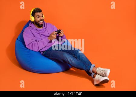 Full size photo of overjoyed man sit bag hand hold controller play games isolated on orange color background Stock Photo