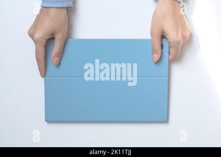 A tablet in a blue case on a white desk. The girl's hands are holding a tablet. top view Stock Photo