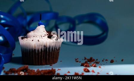 chocolate cupcake with white buttercream and blue candle, dark background and blue ribbon Stock Photo