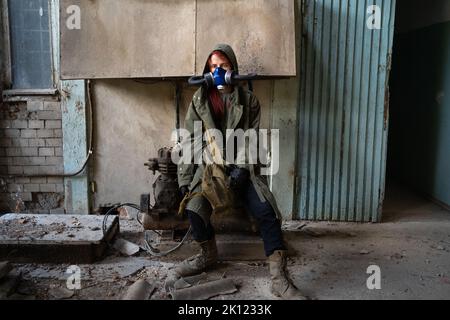 Post apocalyptic female survivor in gas mask, destroyed building in the background. Stock Photo