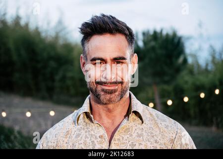 Close Up Portrait of happy mature adult Man Looking and smiling at Camera standing outdoors Stock Photo