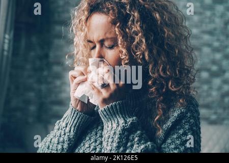 Side view of woman blowing nose for flu influenza symptoms in winter at home. Temperature reduction indoor to save energy gas costs. Female people wit Stock Photo