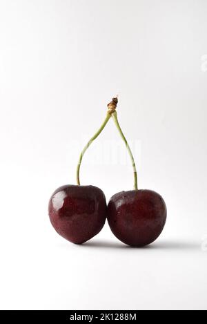 Detail of two joined cherries on white table with white isolated background. Front view. Vertical composition. Stock Photo