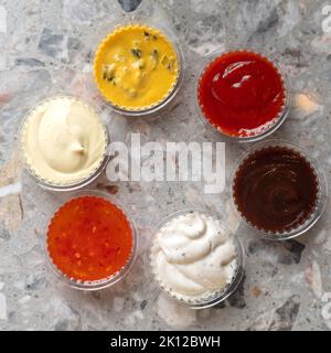 Various sauces and dips in plastic bowls on gray stone background. Copy space Stock Photo