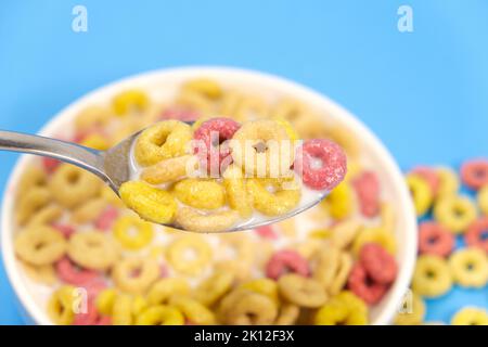 Cereal rings with milk, close-up in spoon, blue background. Stock Photo
