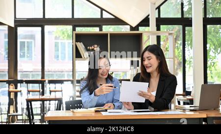 Two beautiful young Asian businesswomen or female marketing workers happy to planning and working on their project together in the office co-working s Stock Photo