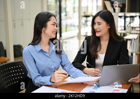 Happy and cheerful young Asian businesswomen or female office workers enjoy talking and having nice conversations during work together. Stock Photo