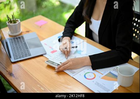 An Asian financial analyst or female accountant using calculator, analyzing business financial and sales data, working on report. top view Stock Photo