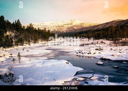 Frozen river in the magic Norwegian Setesdal during winter at sunset. Stock Photo