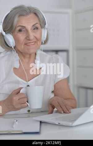 Elderly woman in headphones take online course on computer at home. Stock Photo